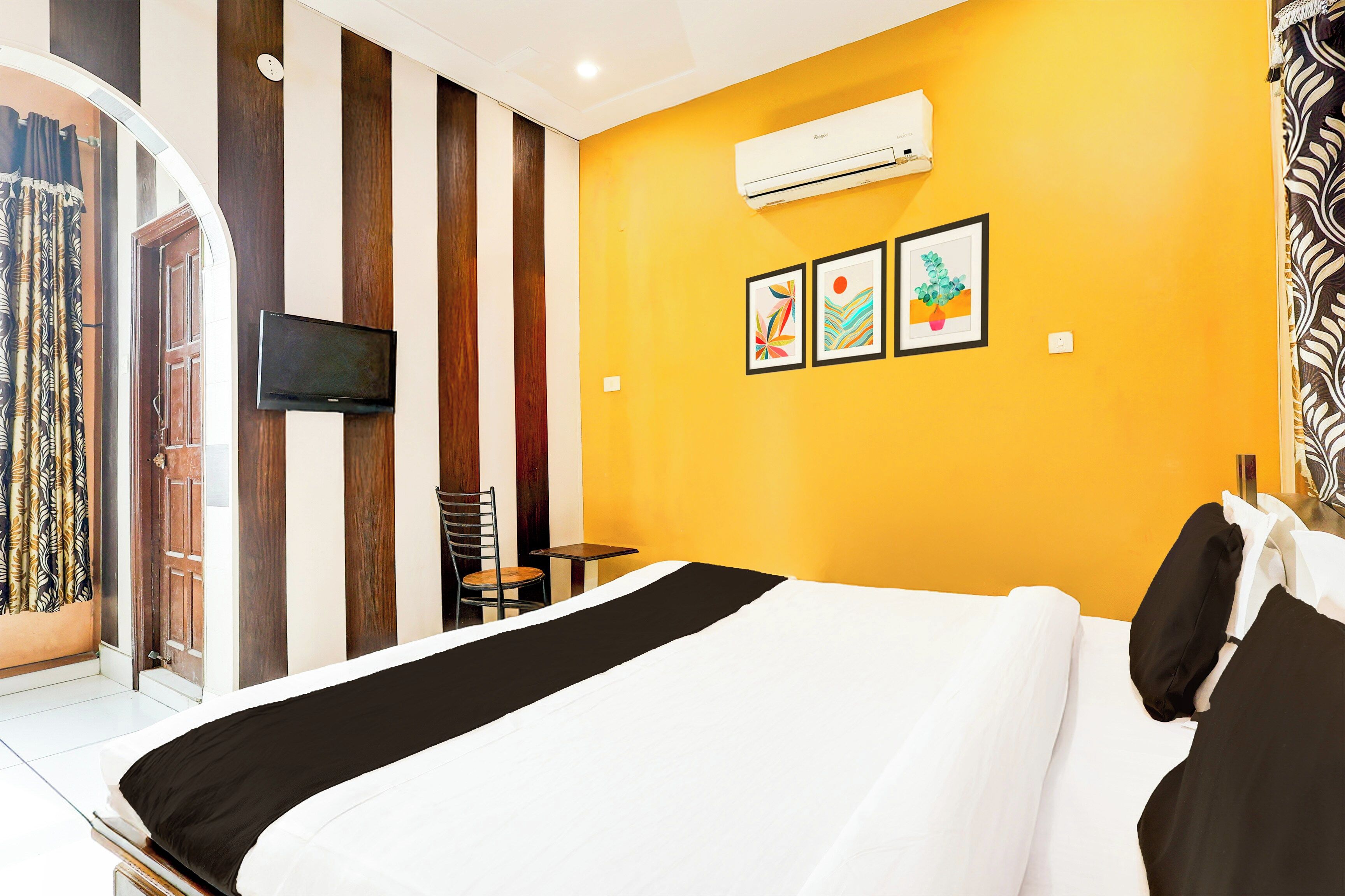 Habitación de hotel con una cama, un televisor montado en la pared y tres obras de arte enmarcadas.