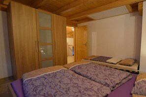 A bedroom with two beds, wooden wardrobe, and a door leading to another room. - Holiday home with 2 bedrooms (Lechbruck am See)