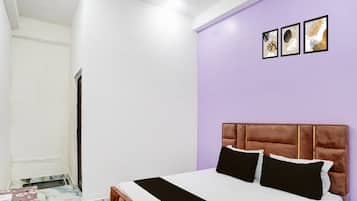Ein Schlafzimmer mit Bett, Schreibtisch und Stuhl. Eine Tür und eine Wand mit Bildern sind ebenfalls vorhanden.