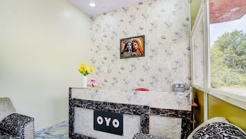 A room with a reception desk labeled 'OYO,' a patterned wall, a window with a view, and a vase with flowers.