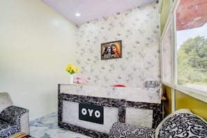 A room with a reception desk labeled 'OYO,' a patterned wall, a window with a view, and a vase with flowers. - Hotel O MN Palace (Jabalpur)