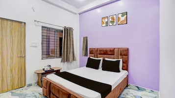 A bedroom with a bed, a window with curtains, a bedside table, and a wall with three framed pictures.