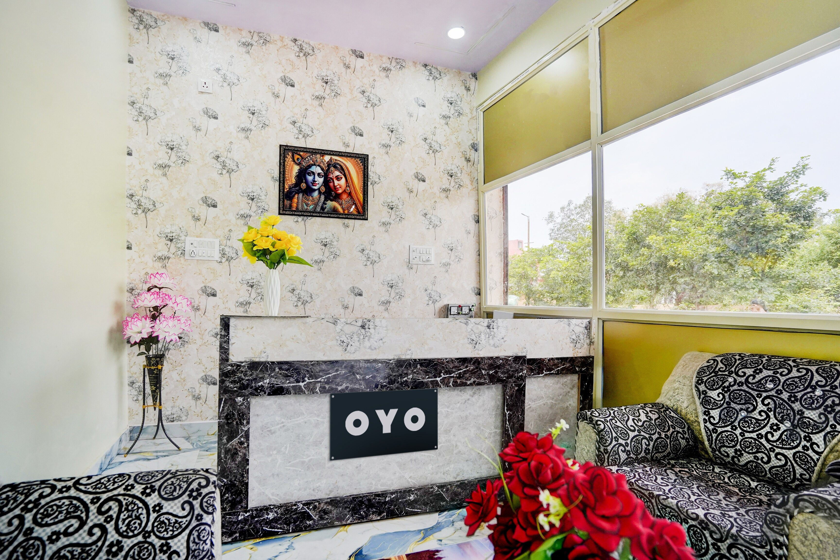 Una habitación con papel tapiz floral, un cuadro en la pared, una chimenea con un letrero y un sofá con cojines estampados.