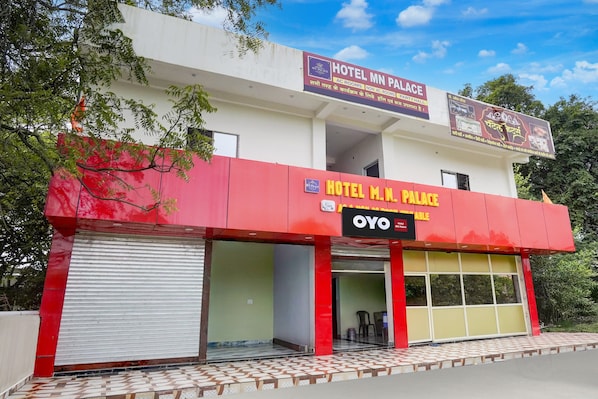 A two-story building with a red and white facade, signs indicating 'Hotel M.N. Palace' and 'Oyo Hotel MN Palace,' and a partially visible entrance. - Hotel O MN Palace (Jabalpur)