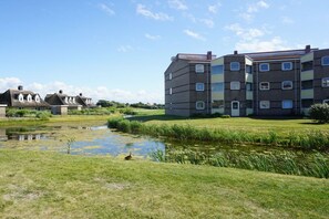 A residential building with multiple floors, a grassy area with a pond, and a clear sky. - Residence Juliana 69 (Julianadorp)