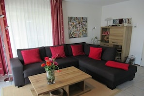 A living room with a black sofa, red cushions, a wooden coffee table, and a wall with a colorful abstract painting. - Residence Juliana 69 (Julianadorp)