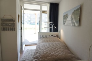 A bedroom with a bed, a window with a view of buildings, a door, and a wall with a picture and a sign. - Residence Juliana 69 (Julianadorp)