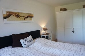 Une chambre à coucher comprenant un lit, une table de chevet, une lampe, une armoire et une œuvre d’art encadrée accrochée au mur.