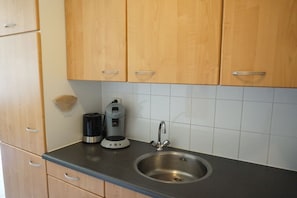 A kitchen with wooden cabinets, a stainless steel sink, and a coffee maker. - Residence Juliana 69 (Julianadorp)