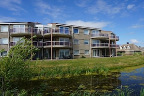 A multi-story residential building with balconies, a grassy area, and a body of water. - Residence Juliana 69 (Julianadorp)