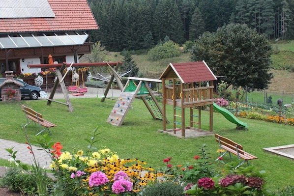 A playground with slides and swings, a wooden playhouse, and a bench. - Morning dew on the Florihof (Tennenbronn)