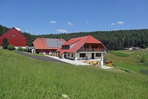 Ein zweistöckiges Haus mit rotem Dach, einem Balkon und einem kleinen Anbau.