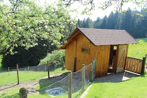 Eine Holzhütte mit geneigtem Dach, umgeben von einem Zaun und einem kleinen Teich.
