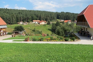 Ein ländliches Dorf mit Häusern, einem Garten und einem bewaldeten Hügel im Hintergrund.