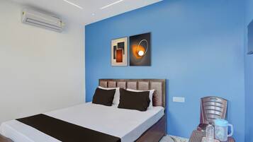 A hotel room with a bed, a nightstand with a water bottle and mug, and a wall-mounted air conditioner.