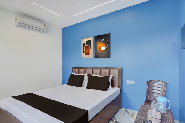 A hotel room with a bed, a nightstand with a water bottle and mug, and a wall-mounted air conditioner. - Hotel O City Point (Jabalpur)