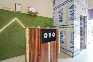 Un comptoir d’accueil avec une enseigne indiquant « OYO », devant un mur vert agrémenté d’un luminaire aux formes géométriques.