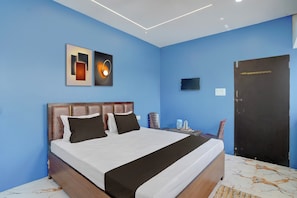 Une chambre d’hôtel avec un lit, une table de chevet, un luminaire fixé au mur et une porte.