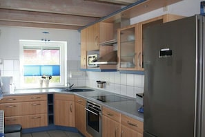 Eine Küche mit Holzausstattung, einem Edelstahlkühlschrank, einem eingebauten Backofen und einem Fenster mit Jalousien.