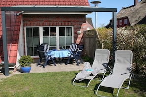 Eine Terrasse mit Tisch und Stühlen, einem kleinen Topfpflanzen und einem überdachten Bereich.
