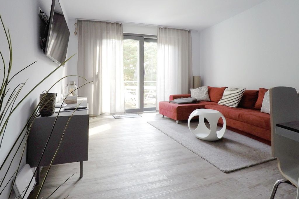 Un salon moderne avec un canapé rouge, une table basse blanche et un téléviseur à écran plat fixé au mur.