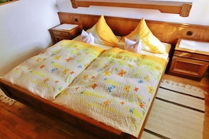 Ein Bett mit blumigem Überwurf, einem Holz-Kopfbrett, zwei Nachttischen und einem Beistelltisch.