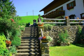 A stone staircase leading to a building with a balcony, surrounded by lush greenery and flowers. - Holiday apartment with 2 bedrooms (Ofterschwang)