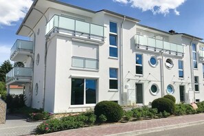A modern two-story building with balconies, large windows, and a well-maintained garden. - Timmare III "Porthole" (Timmendorfer Strand)