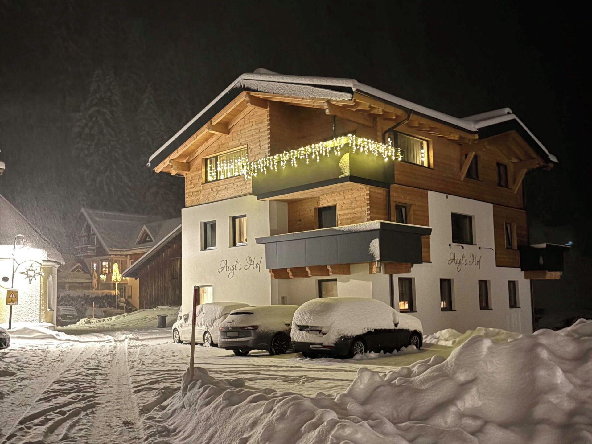 A multi-story building with a balcony, snow-covered cars, and a sign that reads 'Angels Hof.'
