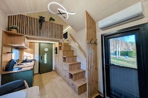 Ein kompakter, moderner Innenraum mit Küchenbereich, einer Holztreppe und einem großen Fenster mit Blick ins Freie.