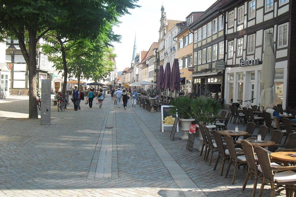 Eine Kopfsteinpflasterstraße gesäumt von traditionellen Fachwerkhäusern, mit Außenbereichen zum Sitzen und wenigen Fußgängern.