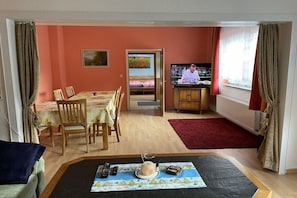 A room with a dining table, chairs, a TV, and a bed with a view of a field. - Holiday home in Blomberg with swimming pool (Blomberg)