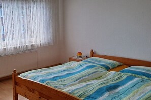 A room with a wooden bed, a nightstand with a lamp, and a window with sheer curtains. - Holiday home in Blomberg with swimming pool (Blomberg)