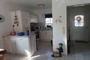 A kitchen with white cabinets, a microwave, and a sink. There is a small dining table with chairs. - Holiday home in Neßmersiel with Wi-Fi (Neßmersiel)