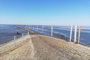 A coastal walkway with a stone surface, metal railing, and wooden posts. - Holiday home in Neßmersiel with Wi-Fi (Neßmersiel)