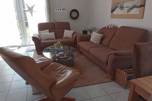 A living room with a brown leather sofa, a glass coffee table, and a small potted plant. - Holiday home in Neßmersiel with Wi-Fi (Neßmersiel)