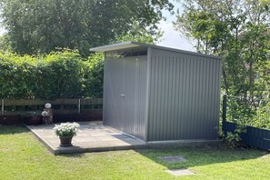 A small, single-story shed with a flat roof and a door, situated in a backyard with a paved patio area. - Holiday home in Neßmersiel with Wi-Fi (Neßmersiel)