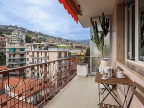 Ein Balkon mit Blick auf eine Wohngegend, einem Kaktus und einem Tisch mit Tassen und einer Kaffeekanne.