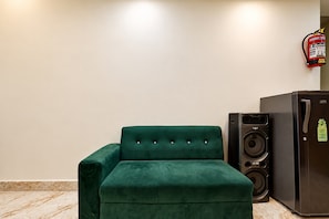 A green upholstered chair and a black refrigerator in a room with white walls and a marble floor. - Hotel O Pix (Jabalpur)
