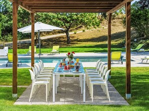 Ein überdachter Essbereich mit Pool im Hintergrund.