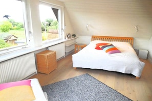 A bedroom with a bed, a window, a radiator, and a wicker chair. - Holiday home with 3 bedrooms (Westerholz)