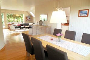 A dining area with a wooden table, chairs, and a vase of flowers. - Holiday home with 3 bedrooms (Westerholz)