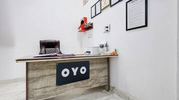 A reception desk with a sign reading 'OYO,' a white wall with framed documents, and a small statue on a shelf.
