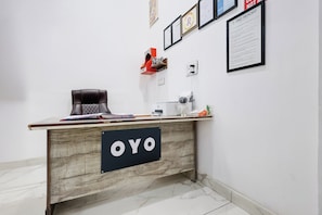 A reception desk with a sign reading 'OYO,' a white wall with framed documents, and a small statue on a shelf. - Hotel O JIND RESORT (Jind)