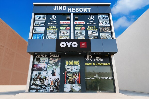 A Jind Resort building with a sign indicating AC rooms available 24/7, a party hall, and a reception area.