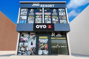 A Jind Resort building with a sign indicating AC rooms available 24/7, a party hall, and a reception area.