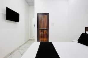 A hotel room with a bed, a flat-screen TV mounted on the wall, a wooden door, and a marble floor.
