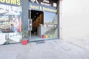 The entrance to a hotel and restaurant with a glass door, potted plants, and a sign indicating the name. - Hotel O JIND RESORT (Jind)