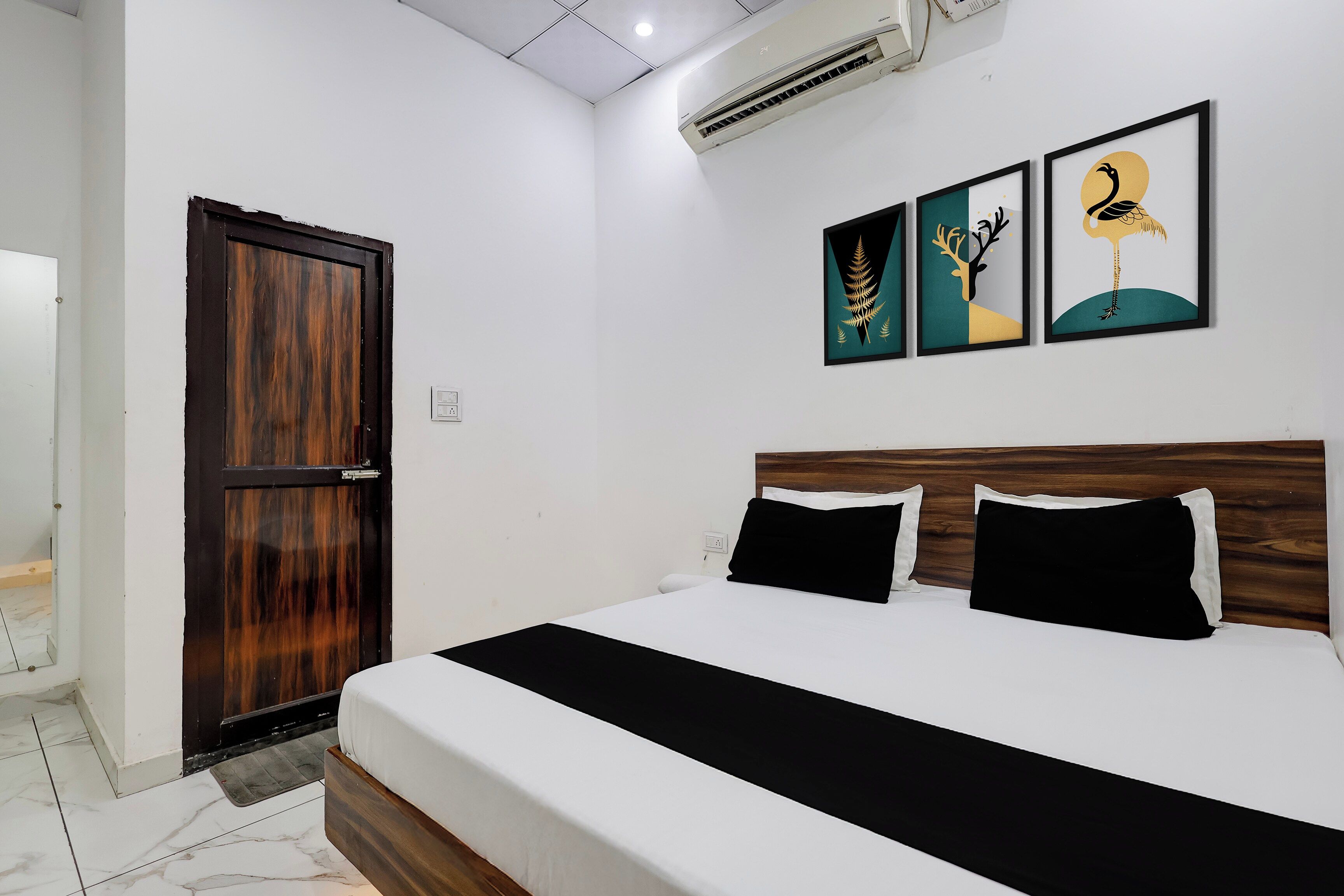 A hotel room with a bed, a wooden door, and three framed artworks on the wall.