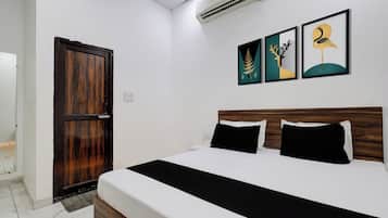 A hotel room with a bed, a wooden door, and three framed artworks on the wall.